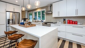 A modern kitchen with white cabinets, a central island with stools, a stainless steel refrigerator, and a gas stove. - 2027 OPEN! Gorgeous Lakeside Home With Pool, Hot Tub, And More! (Lakeside)