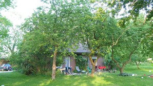 Een huis met gazon, bomen en tuinmeubilair.