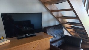 Een flatscreen televisie op een houten kast, een leren bank en een houten trap.