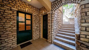 A stone-walled interior with a green door and a staircase leading to an outdoor area.