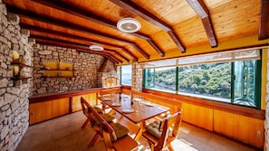 A wooden interior with stone walls, a dining table, and a view of a forested area.