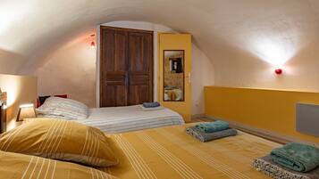 Une chambre avec deux lits, une porte en bois, un miroir et un luminaire fixé au mur.