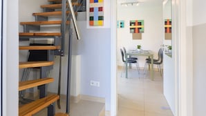 Un interno moderno con una scala in legno, un'area pranzo con sedie e tavolo, e opere d'arte astratte alle pareti.