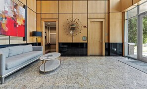 Eine moderne Lobby mit einem grauen Sofa, einem runden Couchtisch und einem großen abstrakten Gemälde an der Wand.