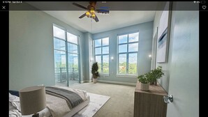 A modern bedroom with a large bed, a bedside table, a ceiling fan, and a view of greenery through large windows. - Long term stay Exquisite penthouse apartment in Raleigh. (Raleigh)