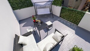 Un balcón con un sofá blanco, una mesita con una planta y un sillón colgante con funda blanca.