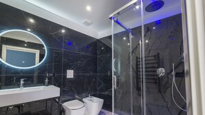 Un baño moderno con ducha envuelta en vidrio, un lavamanos blanco y pared revestida de mármol.
