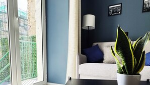 Una sala moderna con un sofá, una mesa con una planta en maceta, una lámpara y vistas al exterior a través de un ventanal grande.