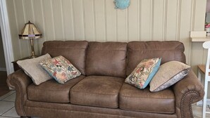 Eine braune Ledersofa mit floralen Kissen, Wandkunst mit einem Wal und einer Schildkröte sowie ein gemustertes Teppich.