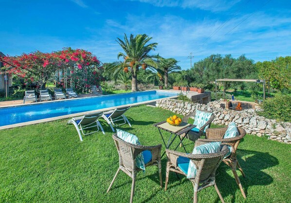 A poolside area with lounge chairs, a table with fruit, and a stone wall.