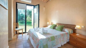 Ein Schlafzimmer mit einem Bett, zwei Nachttischen, einem Sessel und einer Glastür, die zu einem Garten führt.