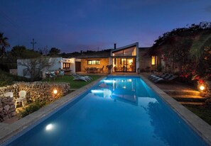 A modern house with a swimming pool, outdoor seating, and a well-lit patio area.