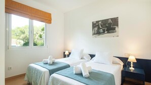 Une chambre d’hôtel avec deux lits, une fenêtre donnant sur un paysage verdoyant, une table de chevet avec une lampe et un tableau accroché au mur.