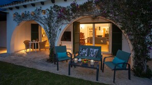 Une terrasse extérieure avec une table et des chaises, un espace salon couvert et une vue sur l’intérieur de la maison.