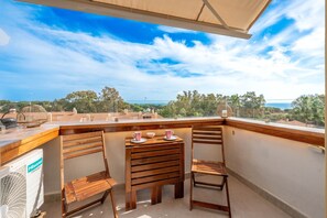 Un balcon avec une table en bois, deux chaises et une vue sur la mer.