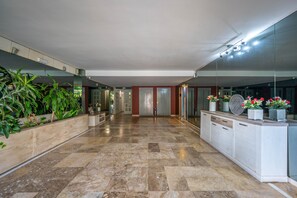 Un hall d’entrée spacieux, doté d’un sol en marbre, d’un comptoir de réception et d’un grand miroir qui reflète l’intérieur.