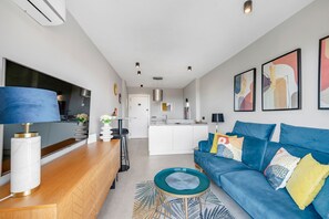 A modern living room with a blue sofa, a coffee table, and a kitchen in the background.
