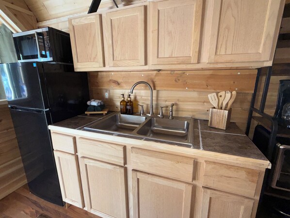 A kitchen with wooden cabinets, a black refrigerator, a double sink, and a microwave.