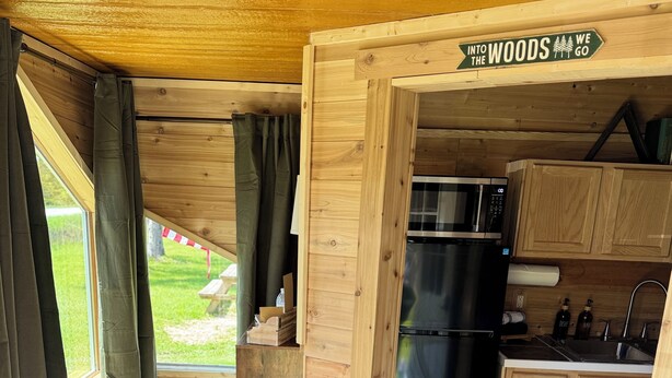 A compact kitchen with wooden cabinets, a microwave, and a refrigerator. - Rustic tiny cabin-WiFi & power, close to beach, boat launch, lighthouse, trails (Rapid River)