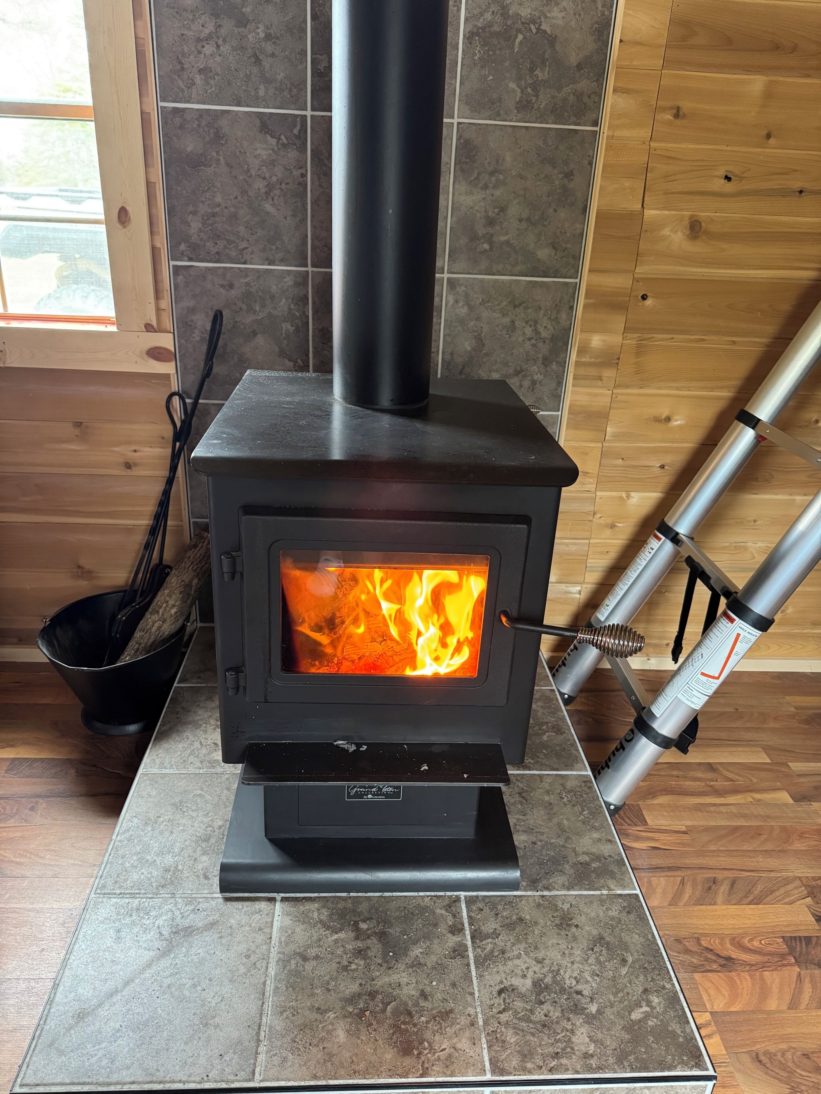 A wood-burning stove with a glass door, a black chimney, and a metal pipe attached to the wall.