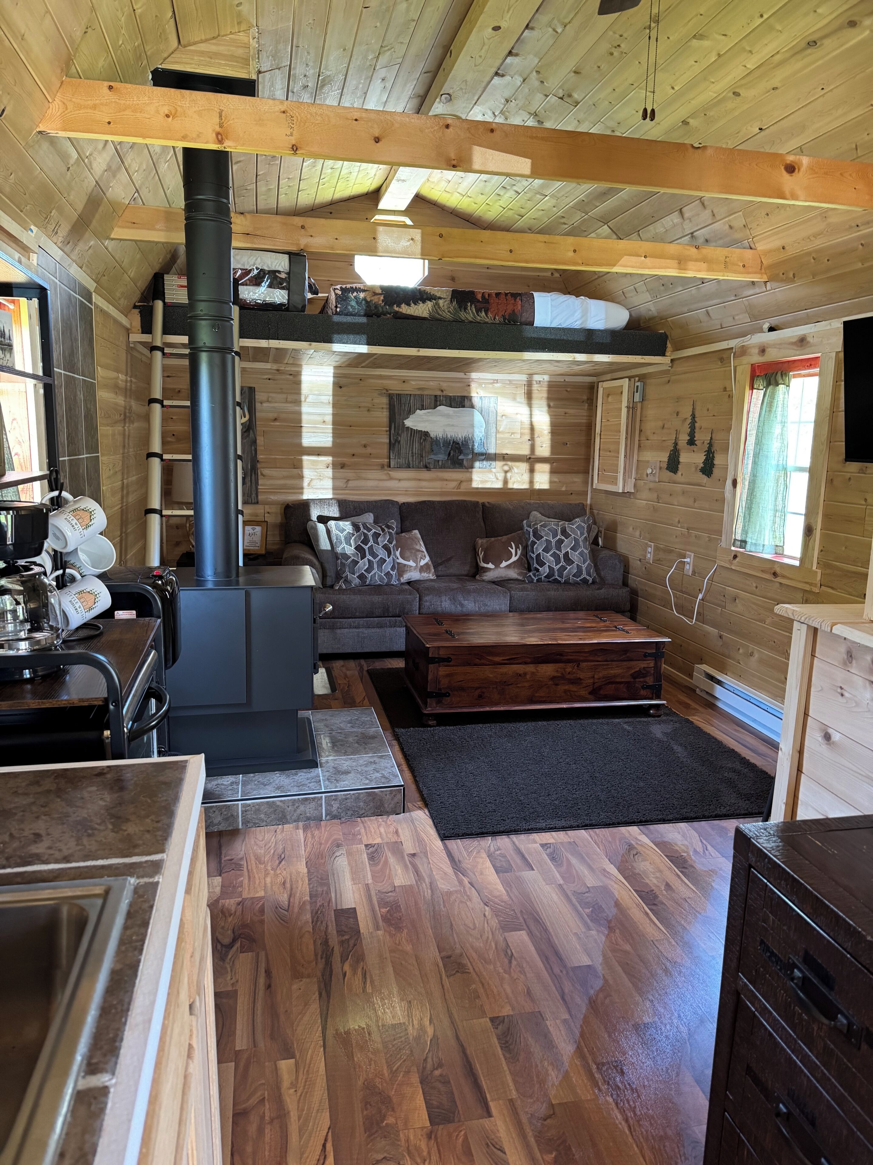 A cozy cabin interior with a fireplace, wooden furniture, and a tiled floor.