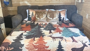 Una habitación acogedora con una cama grande, un sofá gris y una pared de madera con un cuadro.