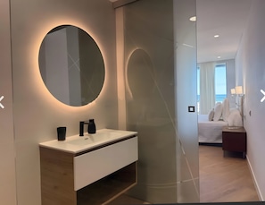 A modern bathroom with a round mirror, a white sink, and a wooden vanity.