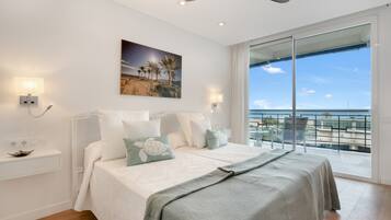 Ein Schlafzimmer mit Bett, Nachttisch, Wandlampe, Gemälde und einem Balkon mit Aussicht.