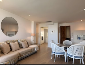 A modern living room with a sofa, a dining table with chairs, a round mirror, and a kitchen in the background.