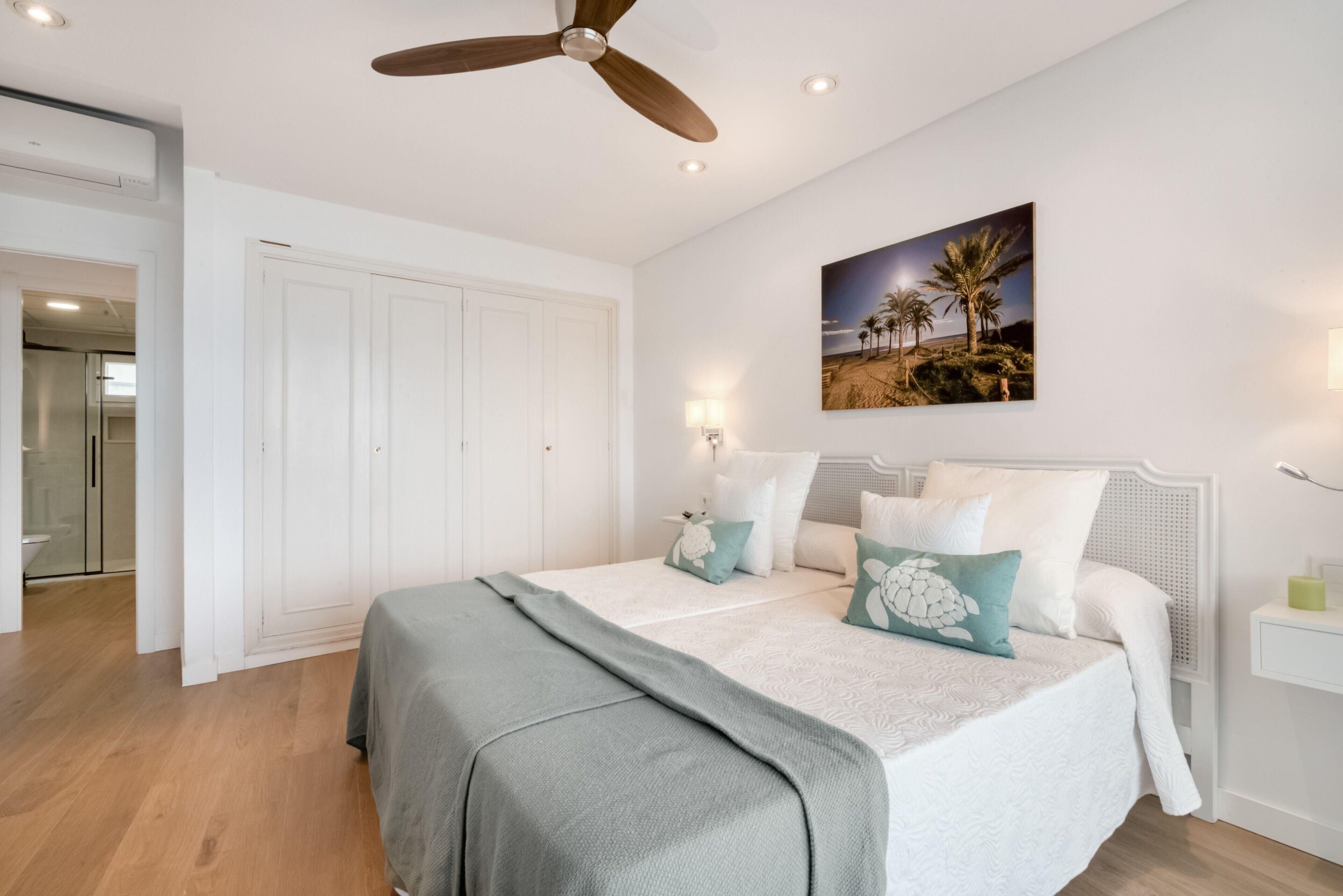 Un dormitorio con cama, ventilador de techo, un cuadro en la pared y una puerta.
