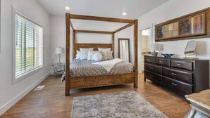 A four-poster bed with a wooden frame, a dark wooden dresser, and a large framed artwork on the wall. - 3BR, 2.5BA Townhome - Great Location + Open-Layout + Modern (Rexburg)