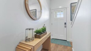 A hallway with a wooden bench, a mirror, a door, and a small plant on the bench. - 3BR, 2.5BA Townhome - Great Location + Open-Layout + Modern (Rexburg)