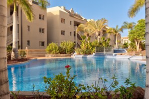 A swimming pool surrounded by palm trees and a building with balconies. - Laderas - FRONT SEA VIEW (Arona)