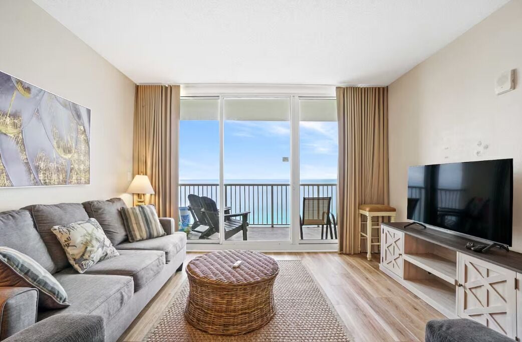 Ein Wohnzimmer mit einer Couch, Sesseln, einem Fernseher und einem Balkon mit Meerblick.