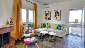 A modern living room with a sofa, two round tables, a fireplace, and a view to the outside. - Theasis Serenity Residence, Secluded Private Pool Retreat with Sea View (Sitia)
