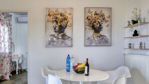 A dining area with a round table, white chairs, and two paintings on the wall. - Theasis Serenity Residence, Secluded Private Pool Retreat with Sea View (Sitia)