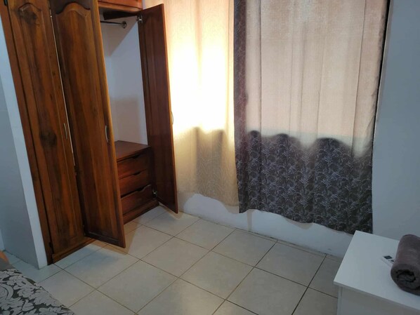 A room with a wooden wardrobe, a small table with a towel, and a window with curtains.