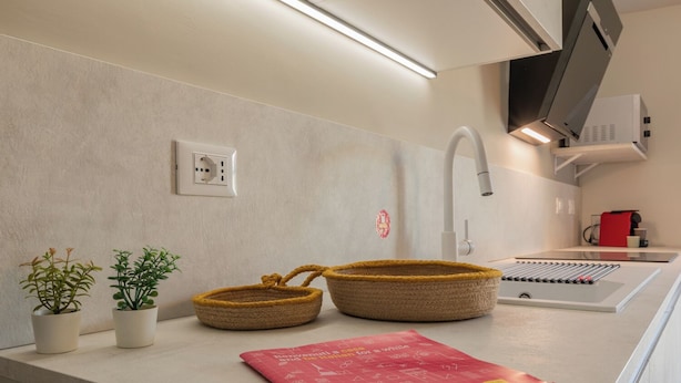 A kitchen counter with a modern design, featuring a built-in stove, a sink, and a microwave. There are two potted plants and a red magazine on the counter. - Casa di Leonardo by Wonderful Italy (Turin)