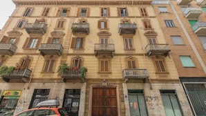 A multi-story building with balconies, a large wooden door, and a storefront with signage. - Casa di Leonardo by Wonderful Italy (Turin)