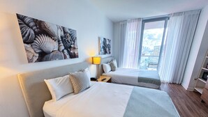 Ein Hotelzimmer mit zwei Betten, einem großen Fenster mit Vorhängen, einer Lampe und Bildern an den Wänden.