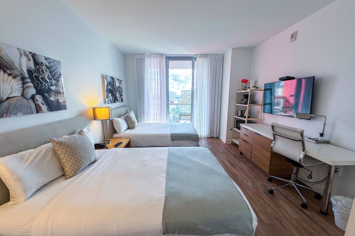 A hotel room with two beds, a desk, a TV, and artwork on the walls.