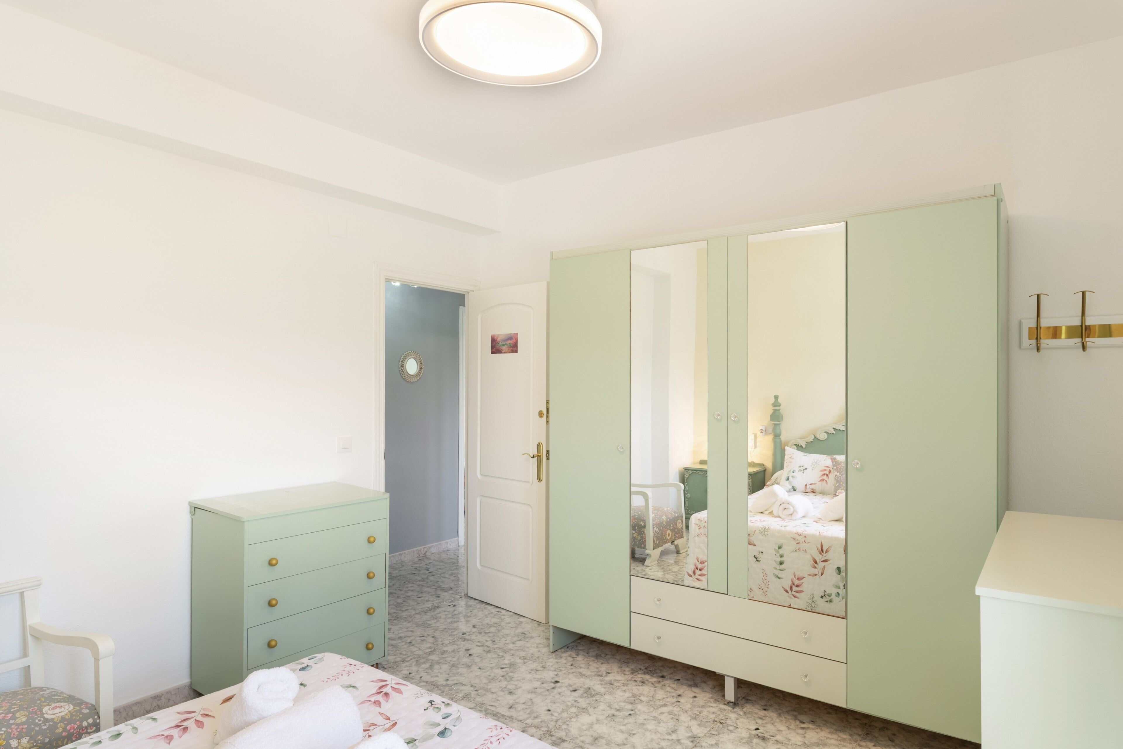 A bedroom with a bed, a dresser, a wardrobe, and a door leading to another room.