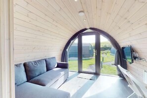 Een knus interieur met een bank, een televisie en een groot raam.