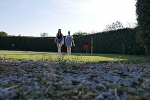 Deux personnes se promènent sur un chemin de gravier, avec une haie et une boîte aux lettres rouge en arrière-plan.