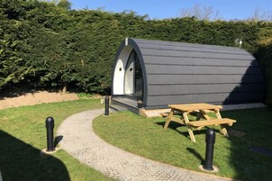 A small, modern, semi-circular structure with a door and windows, adjacent to a wooden picnic table and a paved path.