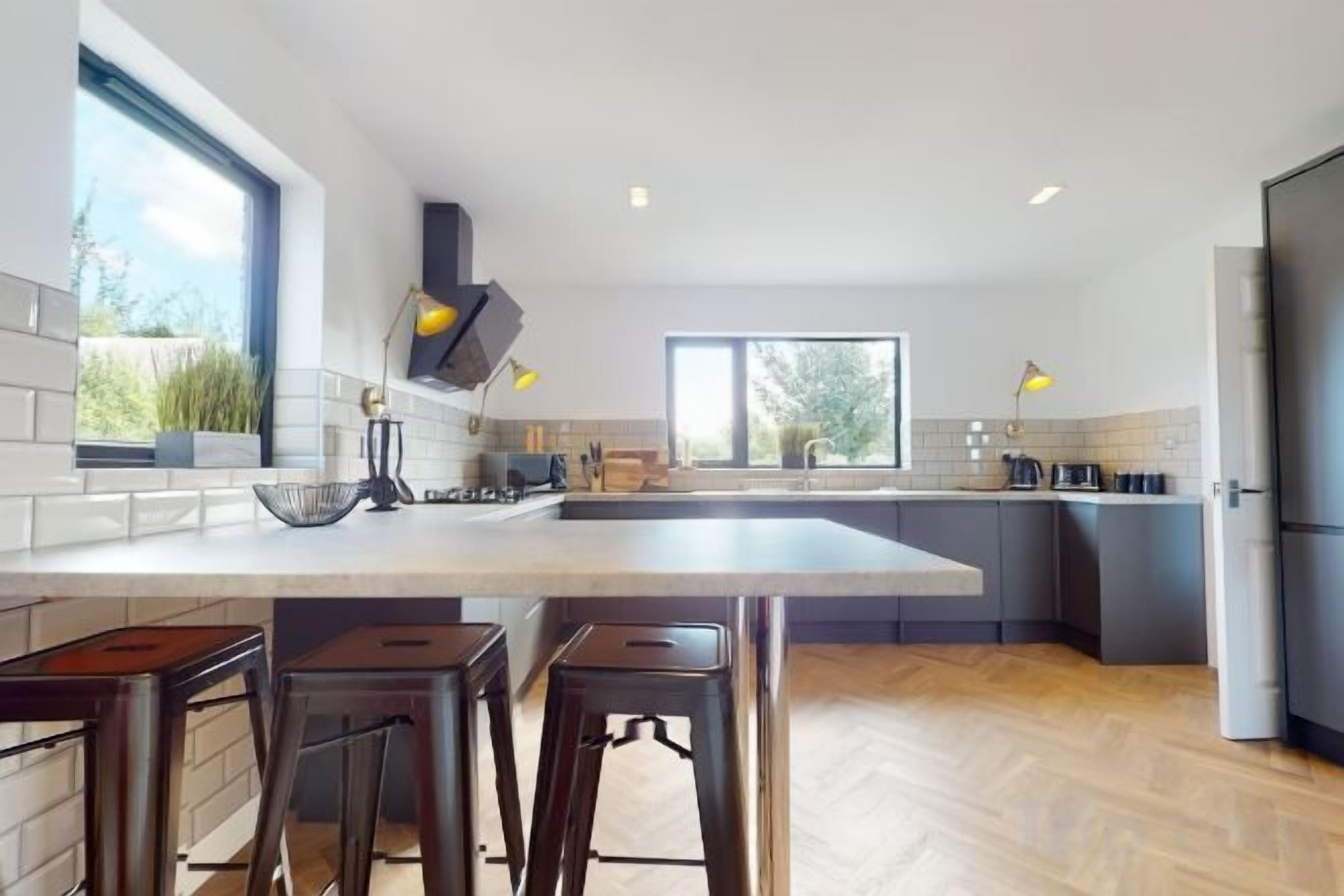A modern kitchen with a large island, bar stools, and a view of the outdoors.