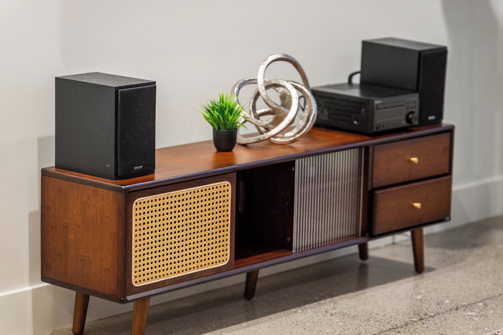 A wooden cabinet with two speakers, a small plant, and a decorative metal ring.