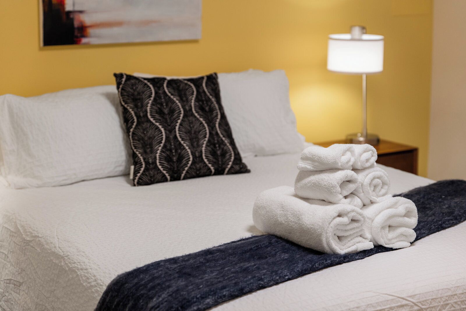 Una cama bien hecha con sábanas blancas, un edredón azul oscuro y una pila de toallas blancas sobre la cama.