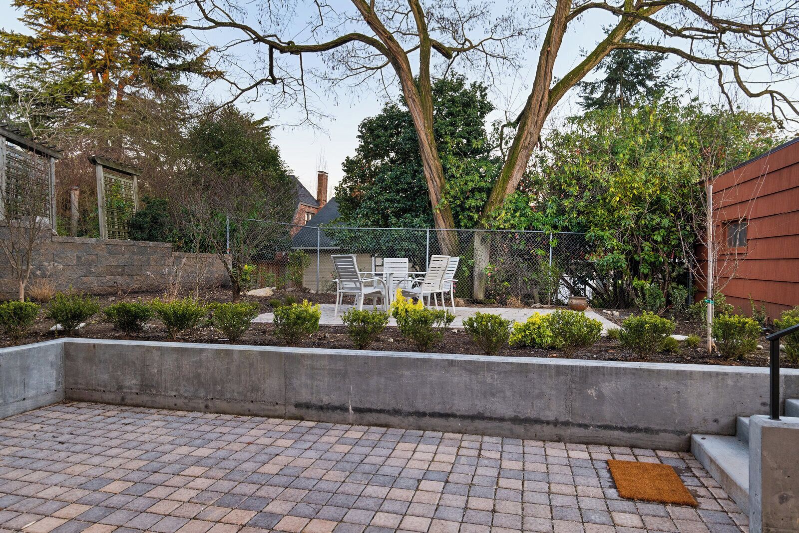 A patio area with a concrete border, a seating arrangement, and a variety of plants and trees.