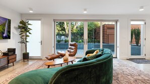 A modern living room with a green sofa, a leather chair, and a coffee table. There is a large window with a view of the outside.